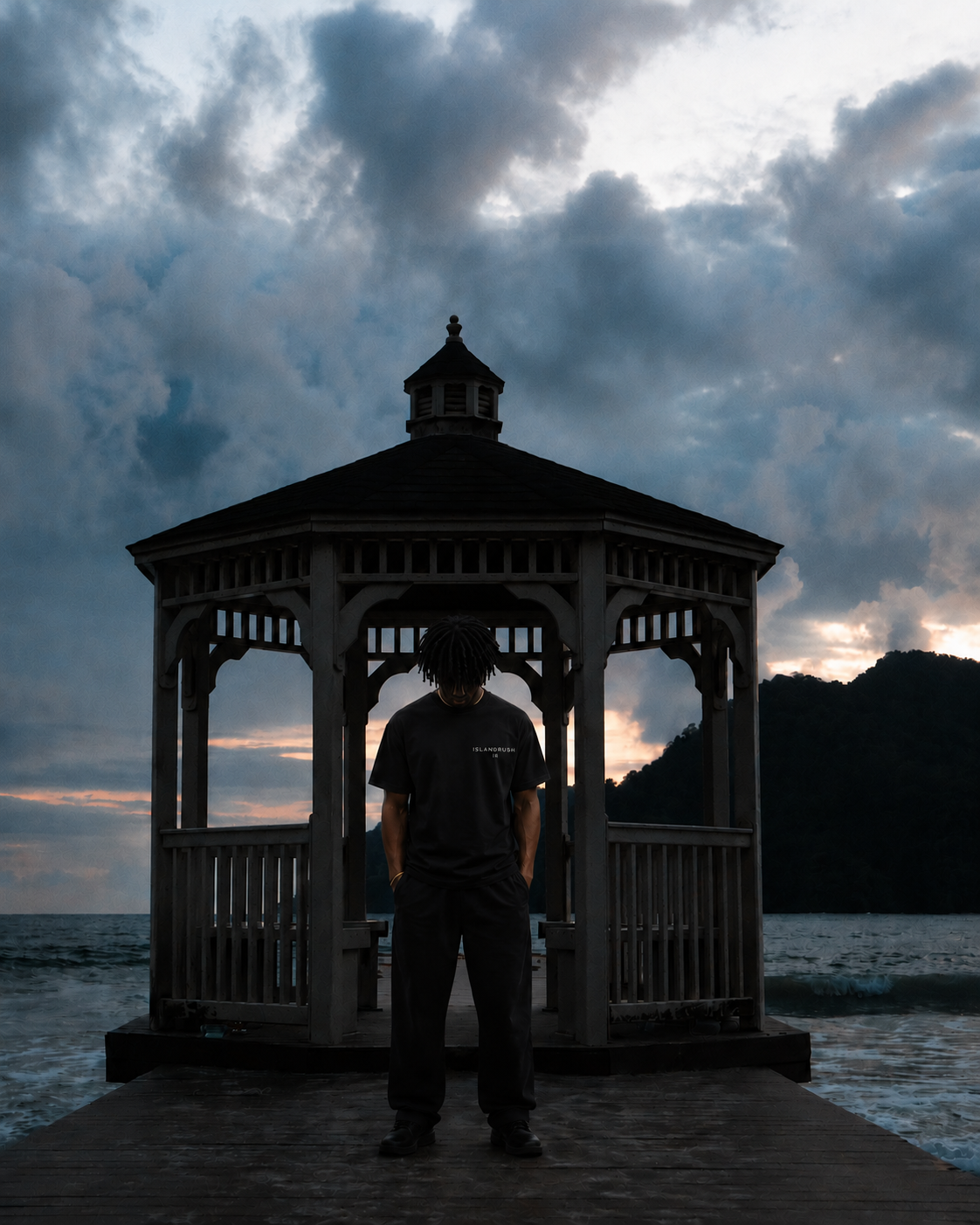 Person standing in front of a wooden gazebo with a dramatic sky and water background